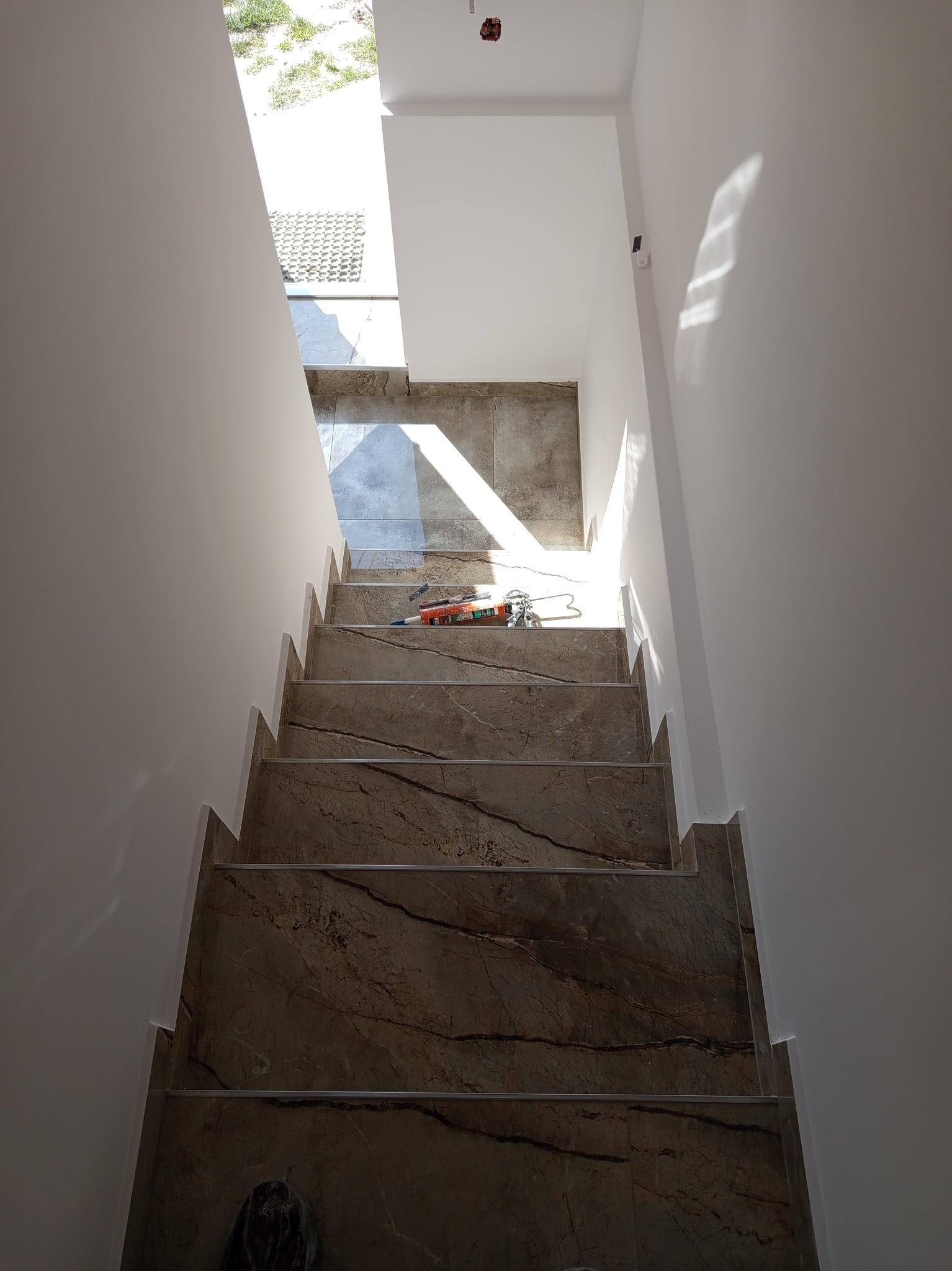 Wykończone schody z płytek imitujących marmur, widok z góry. Na jednym ze stopni leżą narzędzia glazurnicze. Świeżo pomalowane ściany i fragment okna.