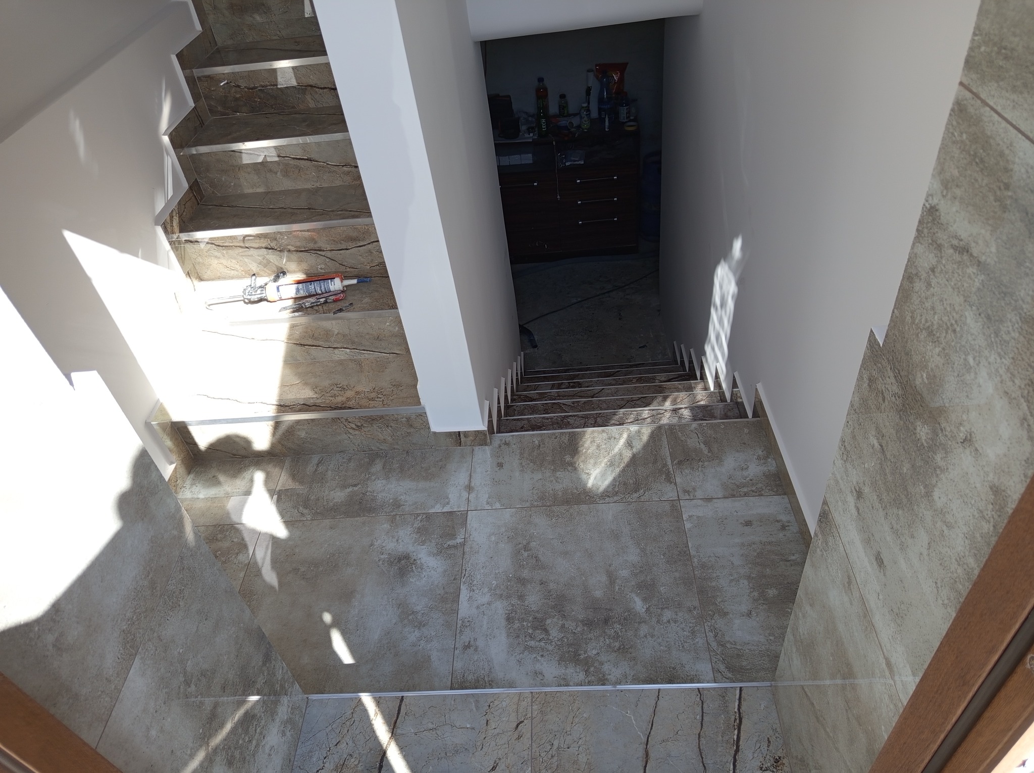 Wykończone schody z płytkami imitującymi marmur, zabezpieczone listwami. Na jednym ze stopni leżą narzędzia i preparaty montażowe. Widok z góry na dół.