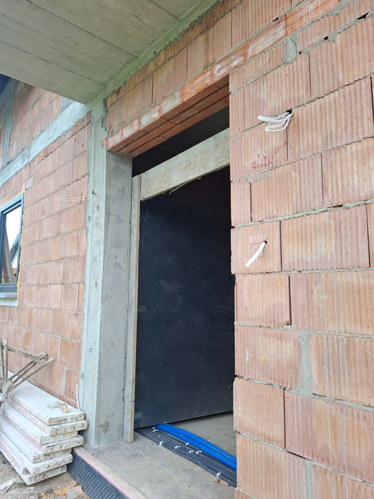 Murowany budynek w Gostyniu w trakcie budowy. Widoczne kable elektryczne wystające ze ściany z czerwonej cegły, przygotowane do dalszych prac.