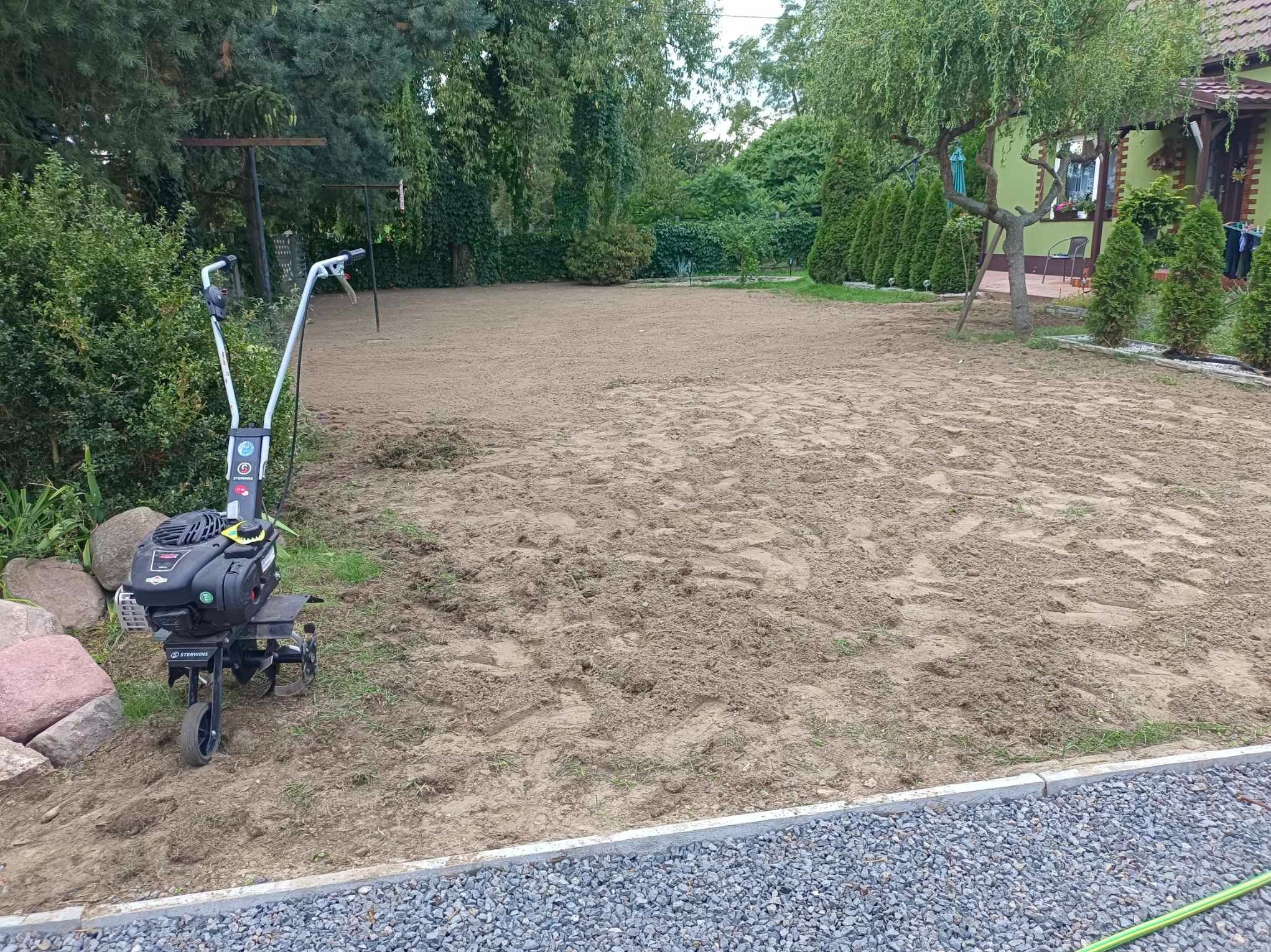 Przygotowany teren pod trawnik, gleba spulchniona glebogryzarką Sterwins, widoczne ślady po maszynie. W tle drzewa i krzewy, obrzeża z kostki. Etap prac ogrodniczych.