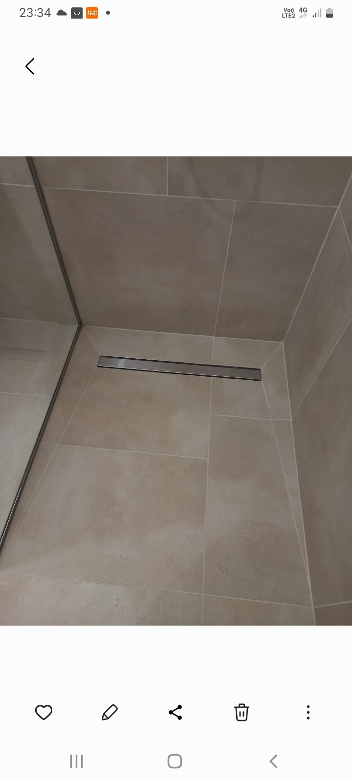 Beżowe płytki w kabinie prysznicowej z odpływem liniowym. Widoczne fugi i chromowane wykończenia.