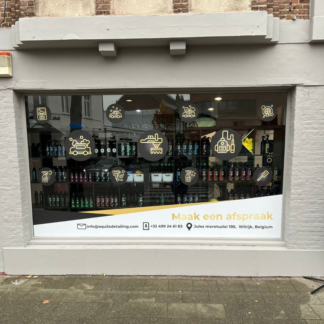 Witryna detailingu z ikonami usług na szkle i danymi kontaktowymi. Widoczne półki z produktami do pielęgnacji aut. Napis: 'Maak een afspraak'.
