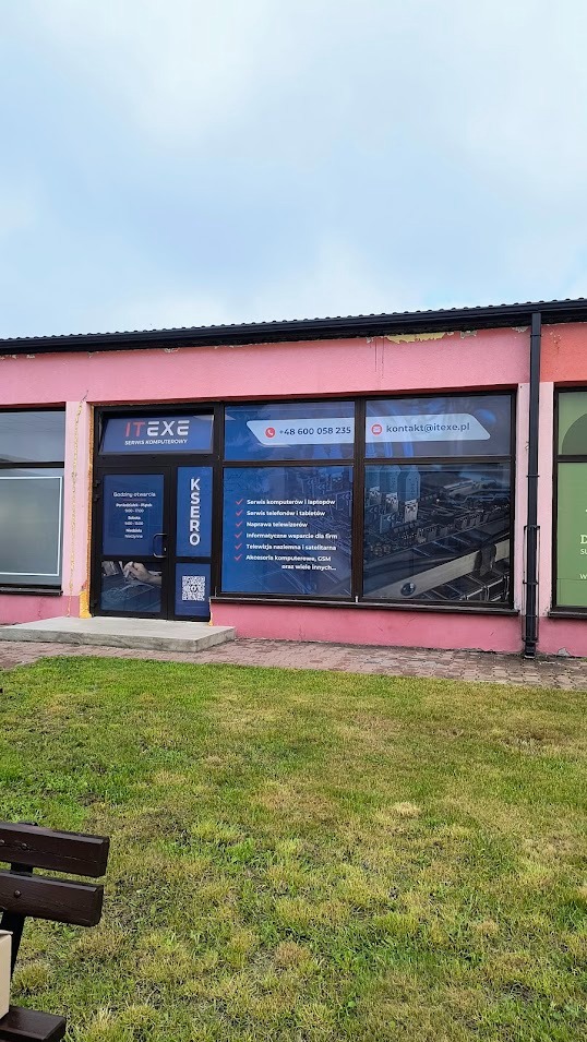 Fasada różowego budynku z logo ITEXE. Na oknach reklamy usług: serwis komputerowy, naprawa telewizorów, wsparcie dla firm. Widoczny numer telefonu i adres e-mail.