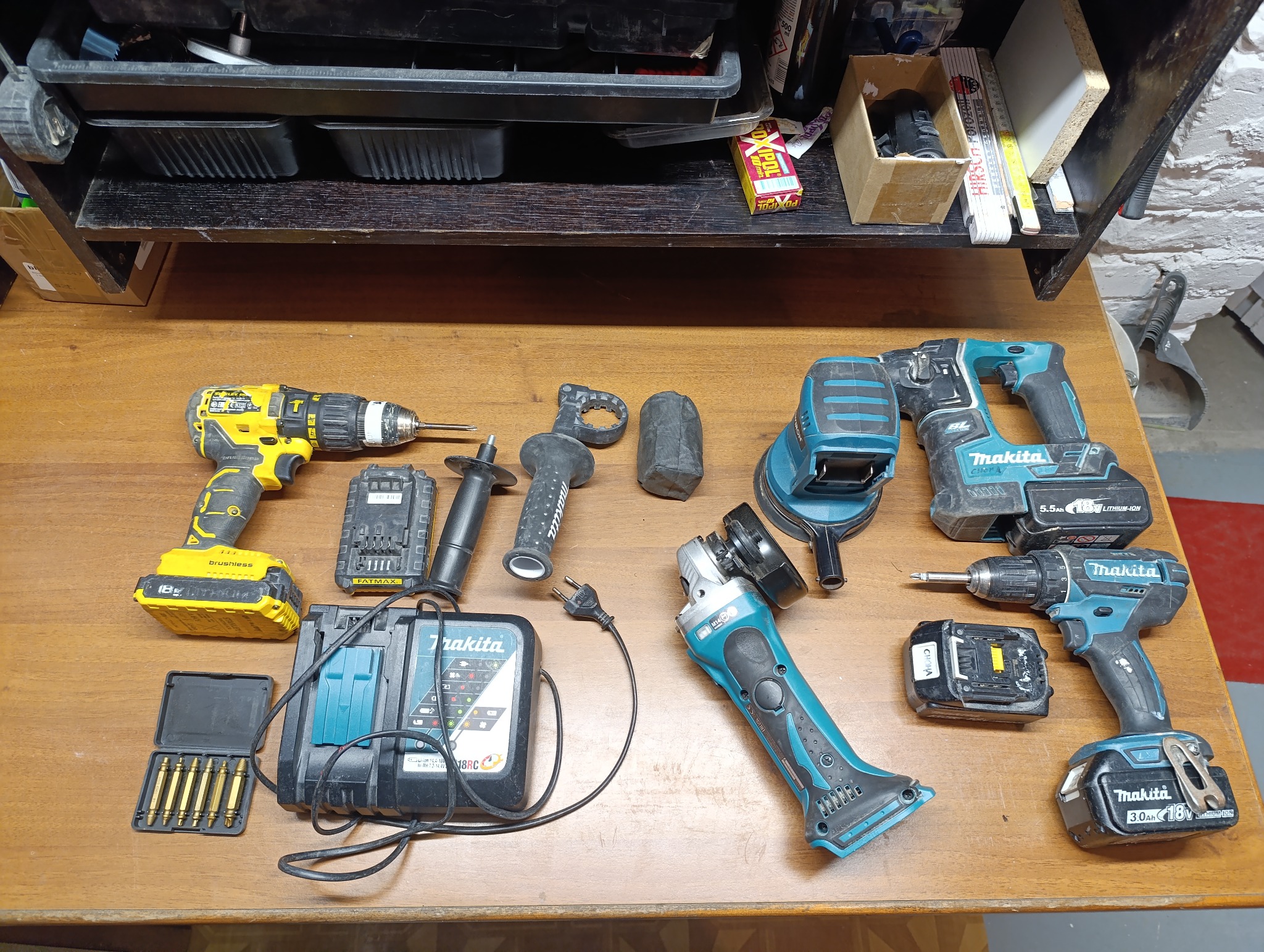 Zestaw narzędzi: wiertarka DeWalt, szlifierka kątowa i oscylacyjna Makita, ładowarka, akumulatory i akcesoria na drewnianym stole warsztatowym.