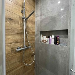 KAFELEK Adam Jaracz - Nowoczesna kabina prysznicowa z drewnopodobnymi i szarymi płytkami, wnęka z kosmetykami. Chromowana armatura i deszczownica. Minimalistyczny design.