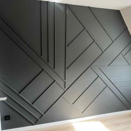 KAFELEK Adam Jaracz - Nowoczesna ściana z geometrycznym wzorem z listew w odcieniach szarości, z widocznym fragmentem podłogi i gniazdkiem elektrycznym.