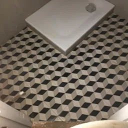 Ukończona podłoga w łazience z geometrycznymi płytkami 3D w odcieniach szarości i czerni, widoczny brodzik. Nietypowy wzór płytek podłogowych.