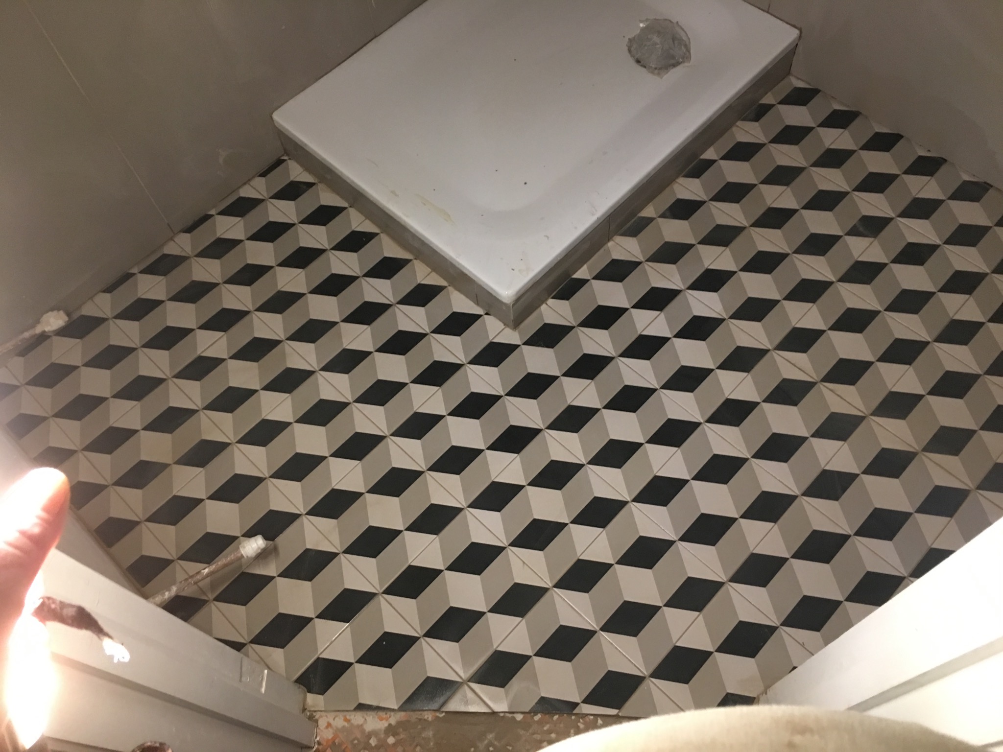 Ukończona podłoga w łazience z geometrycznymi płytkami 3D w odcieniach szarości i czerni, widoczny brodzik. Nietypowy wzór płytek podłogowych.