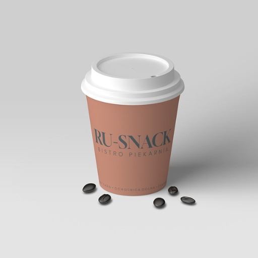 Brązowy kubek z logo 'RU-SNACK Bistro Piekarnia' na białym tle z kilkoma ziarnami kawy. Minimalistyczny design, neutralne oświetlenie.