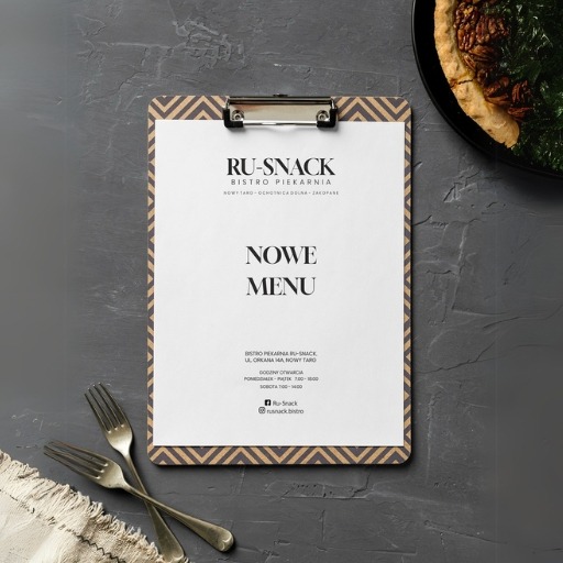 Menu restauracji RU-SNACK na desce z klipsem, obok talerz z daniem i dwa widelce. Minimalistyczny design, ciemne tło z teksturą betonu. Prezentacja oferty.