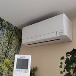 MONTMAR - Biały klimatyzator ścienny Mitsubishi w jasnym wnętrzu, z widocznym pilotem i fragmentem fototapety z motywem leśnym. Ujęcie z dołu.