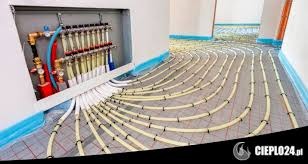 Rozdzielacz ogrzewania podłogowego z rurami ułożonymi w pętle na siatce, widoczne przyłącza i izolacja brzegowa. Instalacja w trakcie montażu przed wylaniem posadzki.