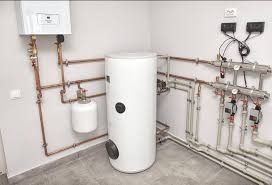 Biały zasobnik ciepłej wody użytkowej z instalacją hydrauliczną w kotłowni w Krakowie. Widoczne rury miedziane i zawory. Nowoczesny system grzewczy.