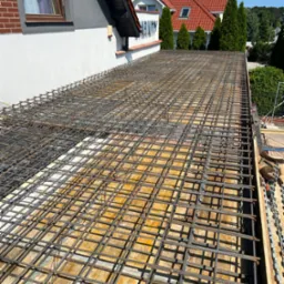 Zbrojenie stropu na deskowaniu, widok z góry, Wołczkowo. Siatka z prętów stalowych przygotowana pod wylewkę betonową. Fragment budynku w tle.