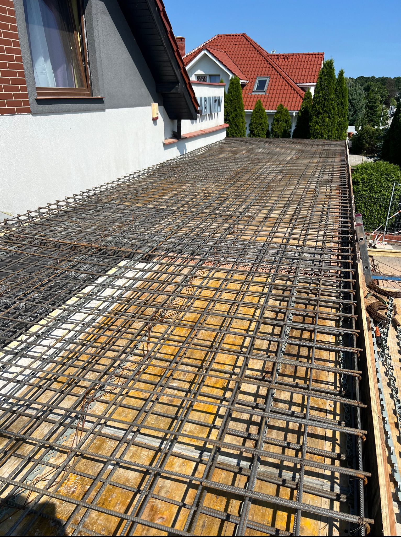 Zbrojenie stropu na deskowaniu, widok z góry, Wołczkowo. Siatka z prętów stalowych przygotowana pod wylewkę betonową. Fragment budynku w tle.