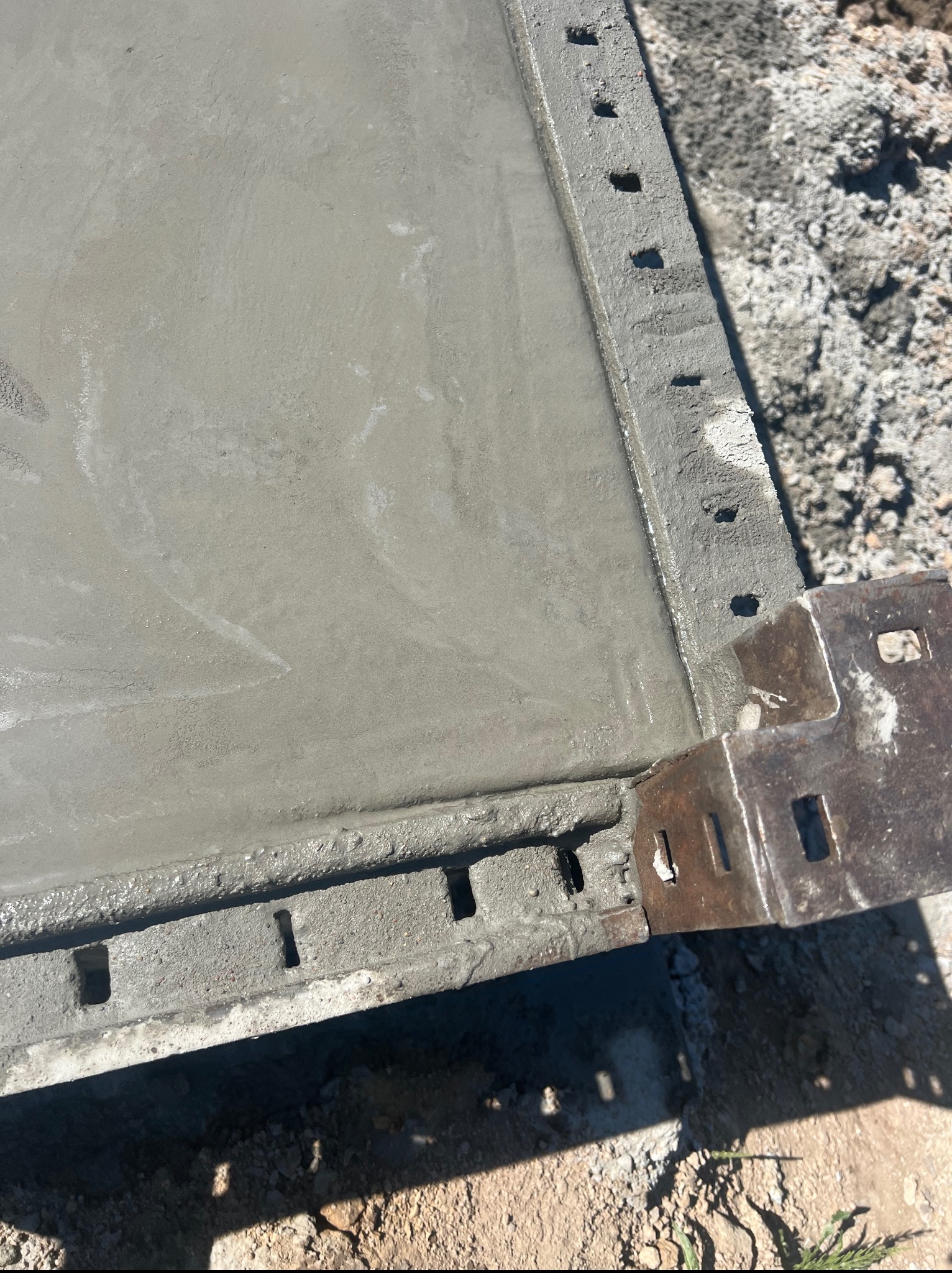 Świeżo wylany beton w szalunku, widoczne detale konstrukcji. Kątowe ujęcie z góry, ukazujące teksturę betonu i elementy szalunku z otworami.