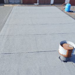 Usługi Dekarskie Maciej Włodarczyk - Szary, płaski dach pokryty papą termozgrzewalną z kominkiem wentylacyjnym i butlą gazową w tle garaży.