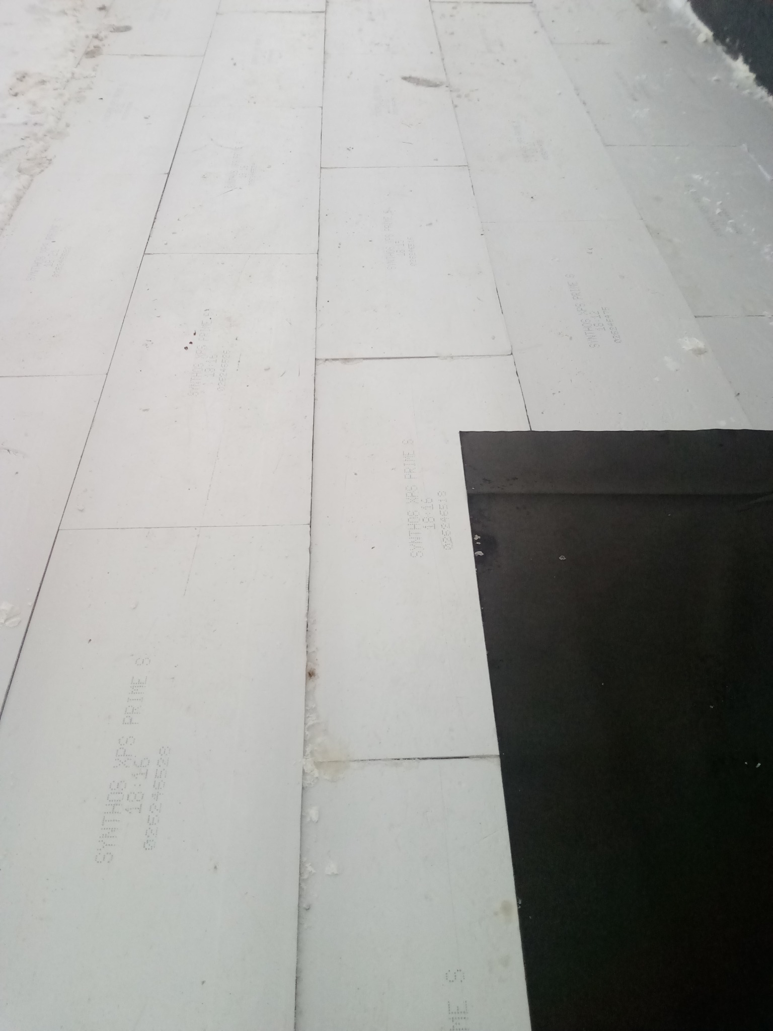 Układanie białych płyt izolacyjnych Synthos XPS Prime S na dachu, częściowo pokrytych czarną membraną. Widok z góry, ukazujący etap prac izolacyjnych.