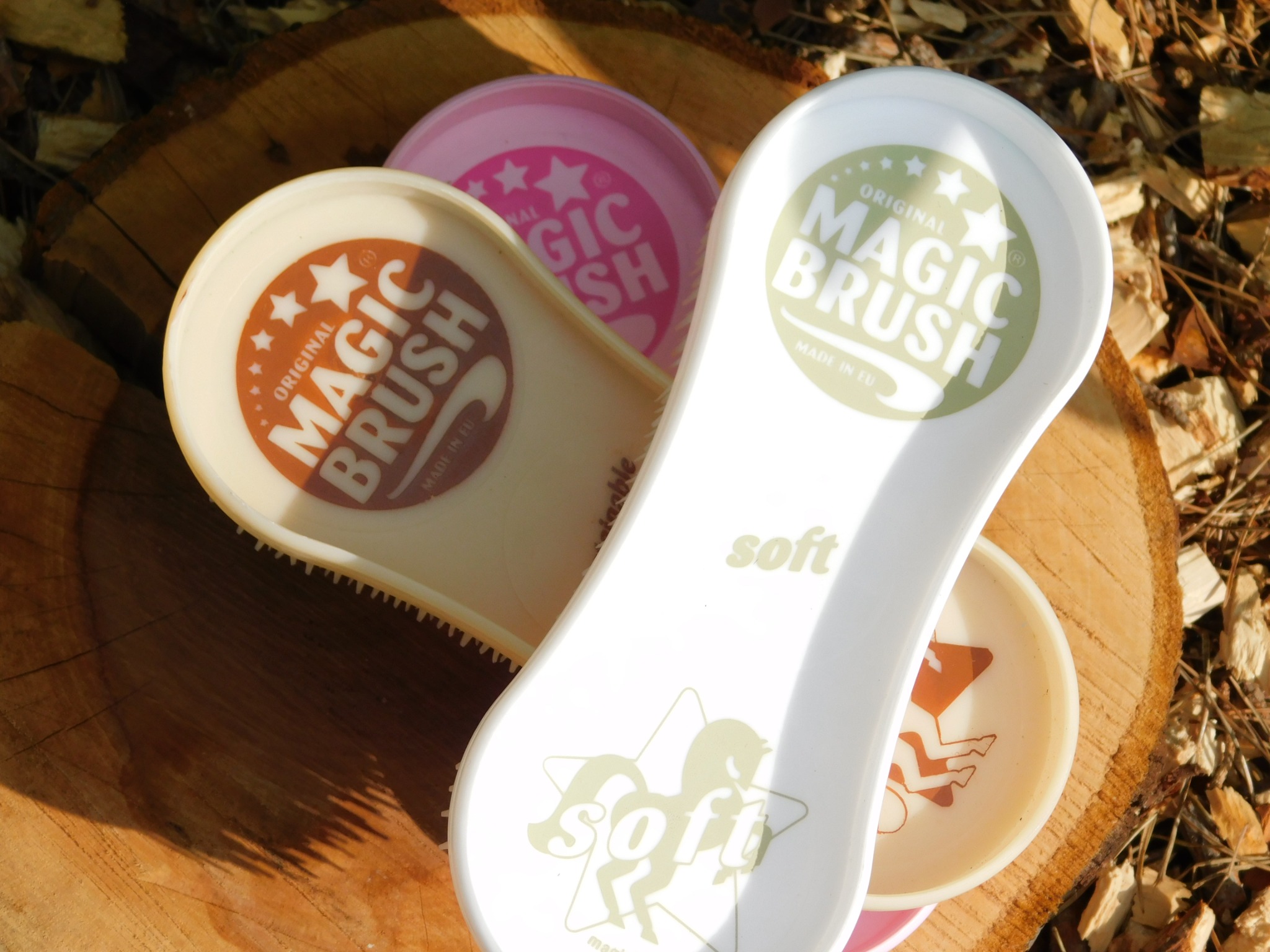 Kolorowe szczotki Magic Brush na tle drewna. Różne kolory i wzory, widoczne napisy 'Original Magic Brush' i 'Soft'. Jasne, naturalne światło, leśny klimat.
