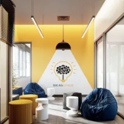 Nowoczesna aranżacja wnętrza biura z żółtą ścianą, grafiką żarówki, pufami i designerskimi stołkami. Minimalistyczne lampy sufitowe i duże okna.