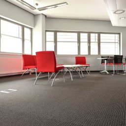 ZALENA GROUP SPÓŁKA Z OGRANICZONĄ ODPOWIEDZIALNOŚCIĄ - Biuro z szarą wykładziną dywanową w jodełkę, czerwonymi krzesłami i dużymi oknami. Widoczny fragment podłogi z dostępem do instalacji.