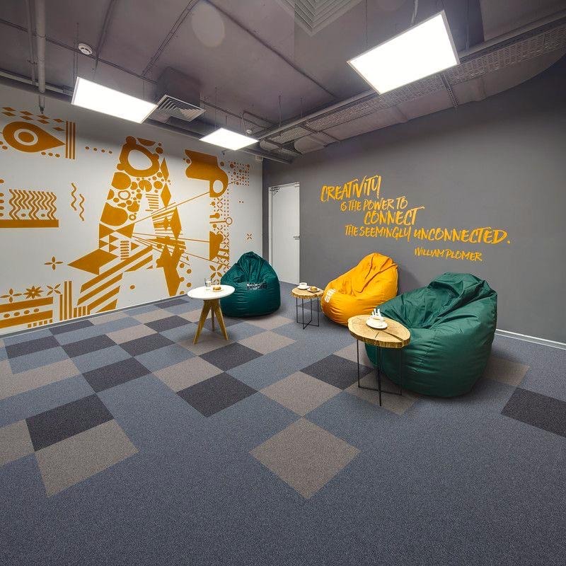 Wnętrze biura z wykładziną w szachownicę, pufami i cytatem na ścianie. Nietypowe, nowoczesne wykończenie podłogi w przestrzeni biurowej. Dekoracyjne malunki na ścianie.
