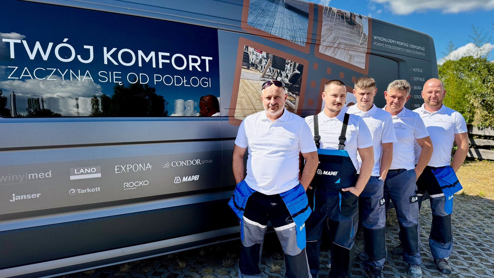 Ekipa montażowa na tle firmowego busa z hasłem 'Twój komfort zaczyna się od podłogi'. Widoczne logotypy producentów. Realizacje dla hoteli i szpitali.