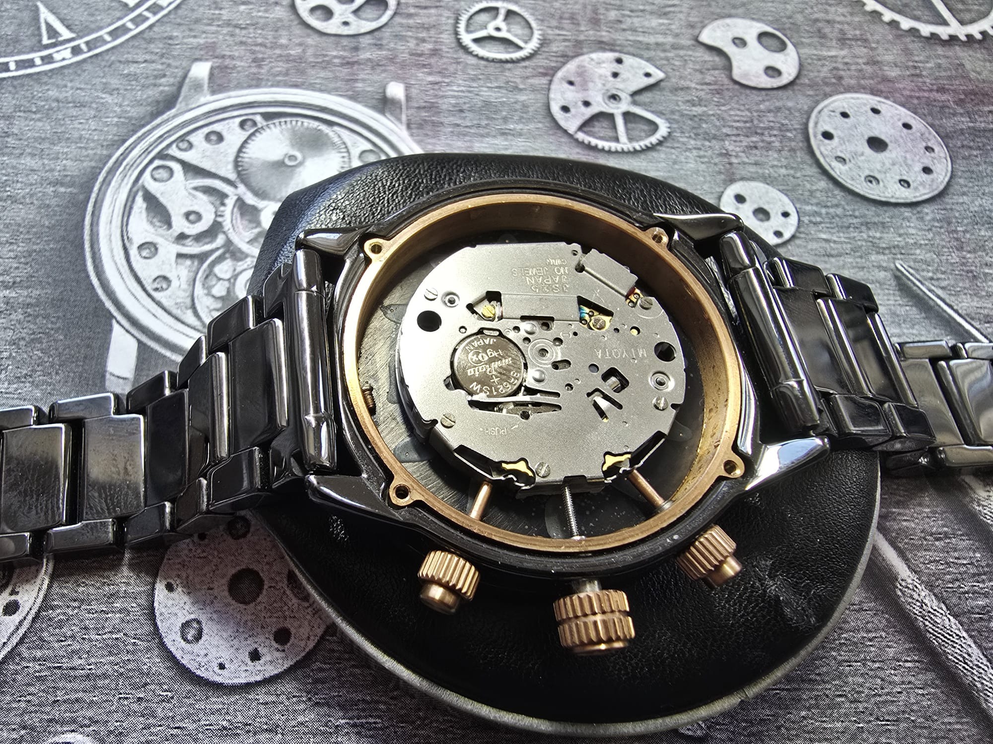 Otwarty, metalowy zegarek na skórzanej podkładce z widocznym mechanizmem i baterią, na tle z grafiką zegarków i trybików. Precyzyjna robota zegarmistrzowska.