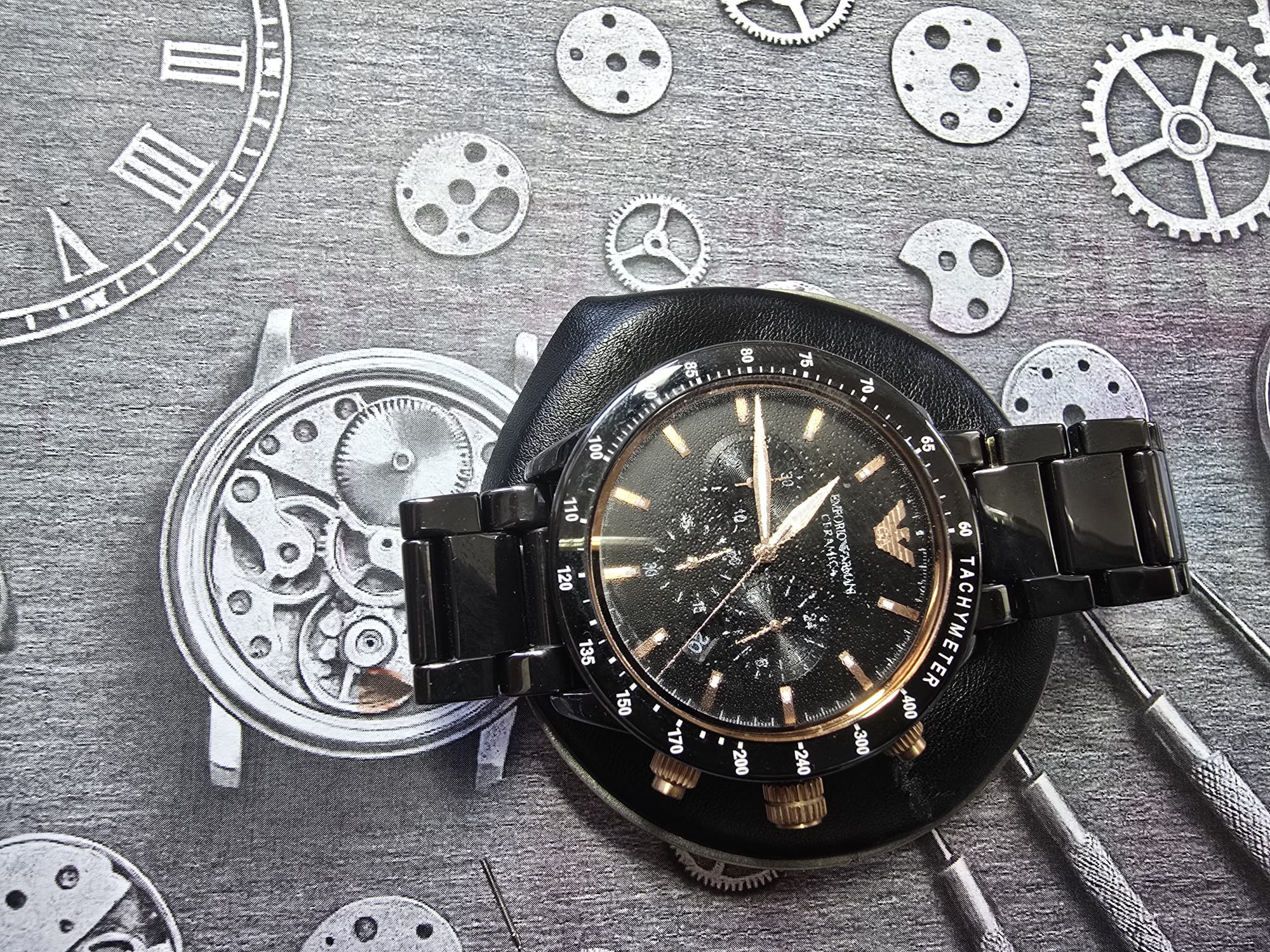 Czarny zegarek Emporio Armani na poduszce zegarmistrzowskiej w Tarnowie, otoczony narzędziami i szkicami mechanizmów. Detaliczne ujęcie na warsztacie zegarmistrza.