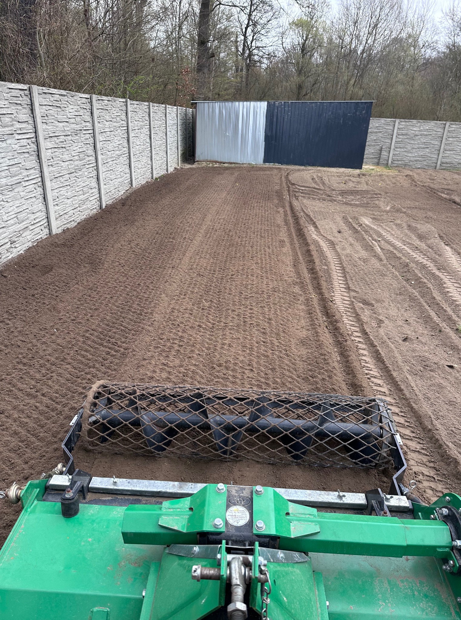 Wyrównywanie terenu walcem siatkowym w Opalenicy. Przygotowanie podłoża pod trawnik. Widoczne ślady opon i wyrównana powierzchnia ziemi.