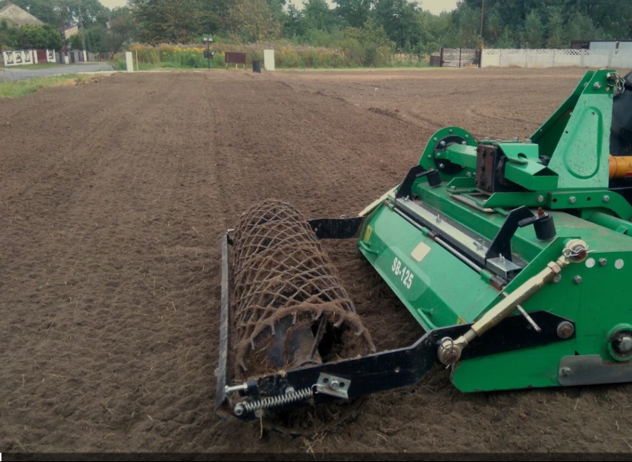Przygotowanie terenu pod trawnik: walcowanie gleby specjalistycznym walcem siatkowym, widoczny fragment maszyny SB-125 i wyrównana powierzchnia ziemi.