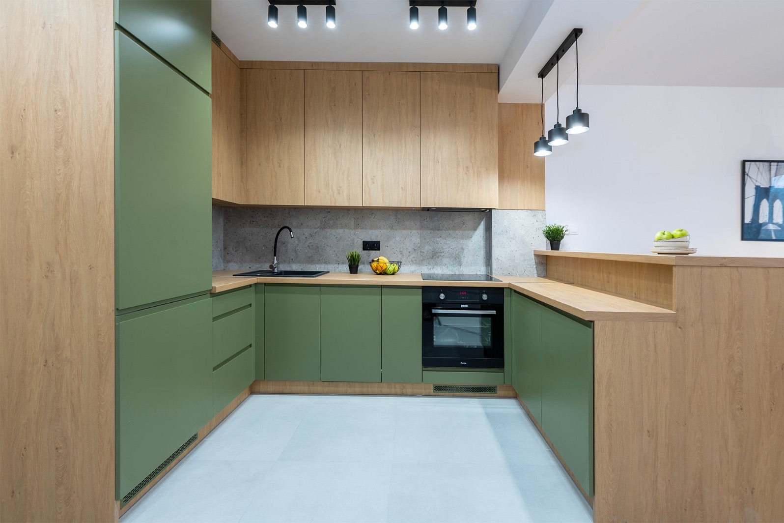 Nowoczesna kuchnia z zielonymi szafkami i drewnianymi blatami. Minimalistyczne oświetlenie, szary backsplash i sprzęt AGD w zabudowie tworzą spójną całość.