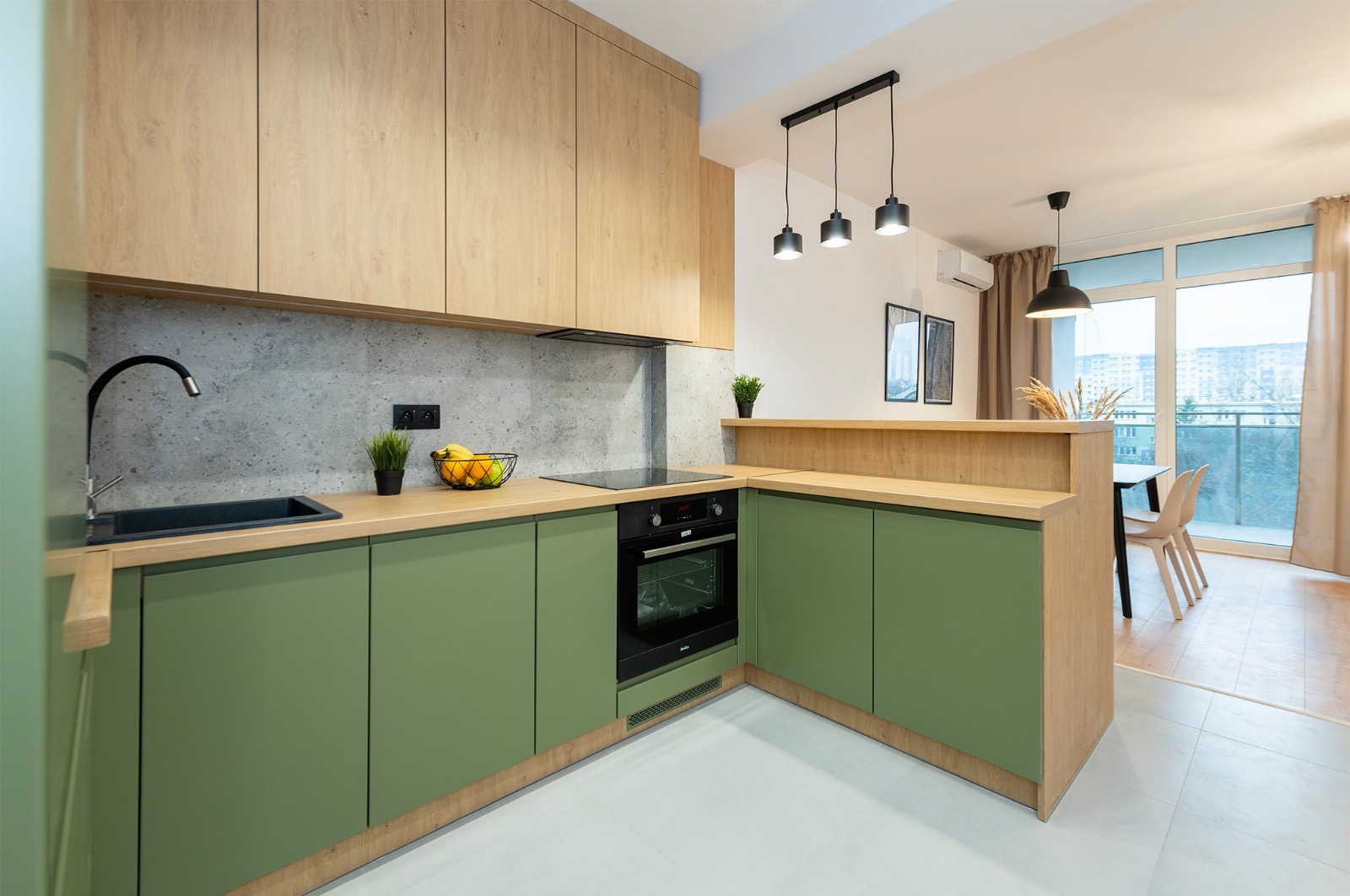 Nowoczesna kuchnia w odcieniach zieleni i drewna, z czarnymi akcentami, oświetleniem i widokiem na balkon. Elementy dekoracyjne, minimalistyczny design.