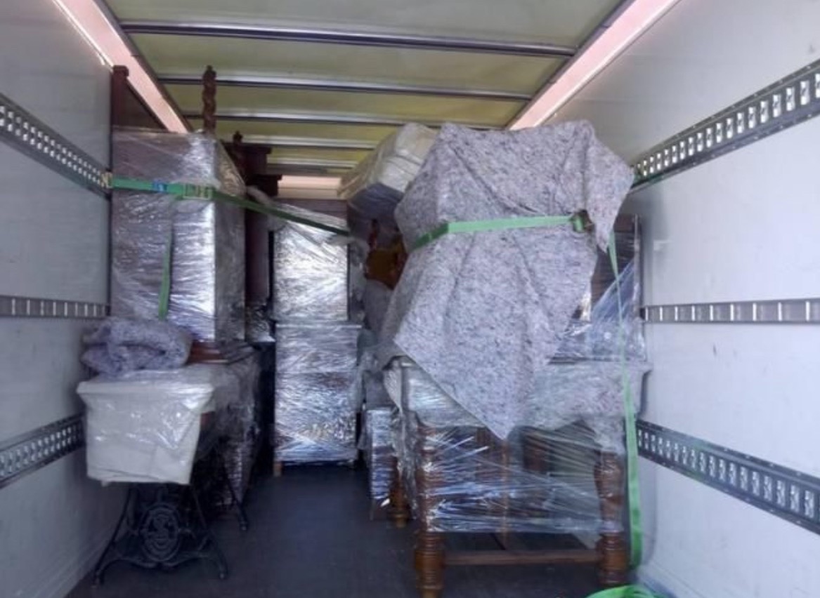 Wnętrze busa wypełnione meblami zabezpieczonymi folią i pasami transportowymi. Widoczna stara maszyna do szycia i komody. Przygotowanie do transportu.