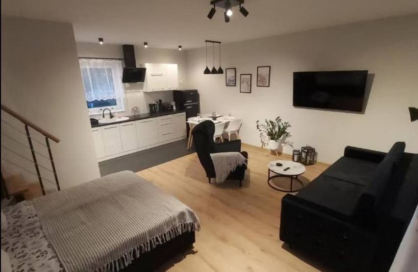 Nowoczesne wnętrze mieszkania z aneksem kuchennym, czarnymi meblami i drewnianą podłogą. Uwagę przykuwa retro lodówka i minimalistyczne oświetlenie.