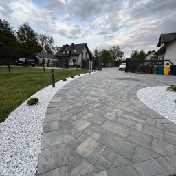 Wykonanie trawnika, wraz z oświetleniem sieciowym zapalanym na czujnik ruchu/zmierzchu lub załączany z włącznika. Całość udekorowana białymi kamieniami zdobionymi. Przestrzeń kamieni i trawy oddzielona obrzeżem.