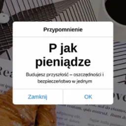 Ekran smartfona z komunikatem 'P jak pieniądze', croissant, kawa i słuchawki na tle gazety. Oszczędności i bezpieczeństwo finansowe w jednym.