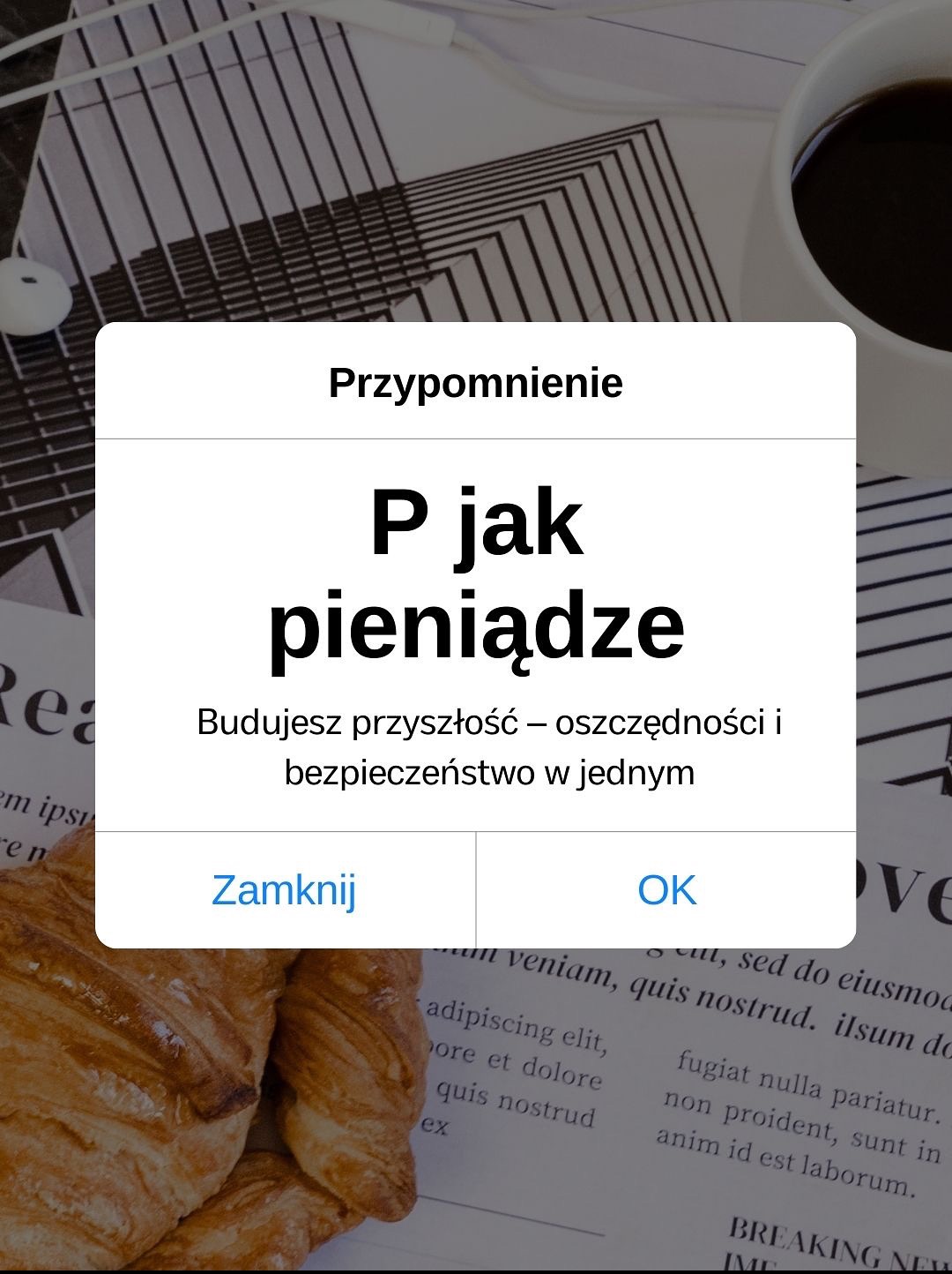 Ekran smartfona z komunikatem 'P jak pieniądze', croissant, kawa i słuchawki na tle gazety. Oszczędności i bezpieczeństwo finansowe w jednym.
