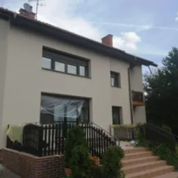 Elewacja domu po renowacji w Tychach, z widocznymi detalami jak okna z roletami i zabezpieczone folią okno. Świeżo pomalowana fasada.