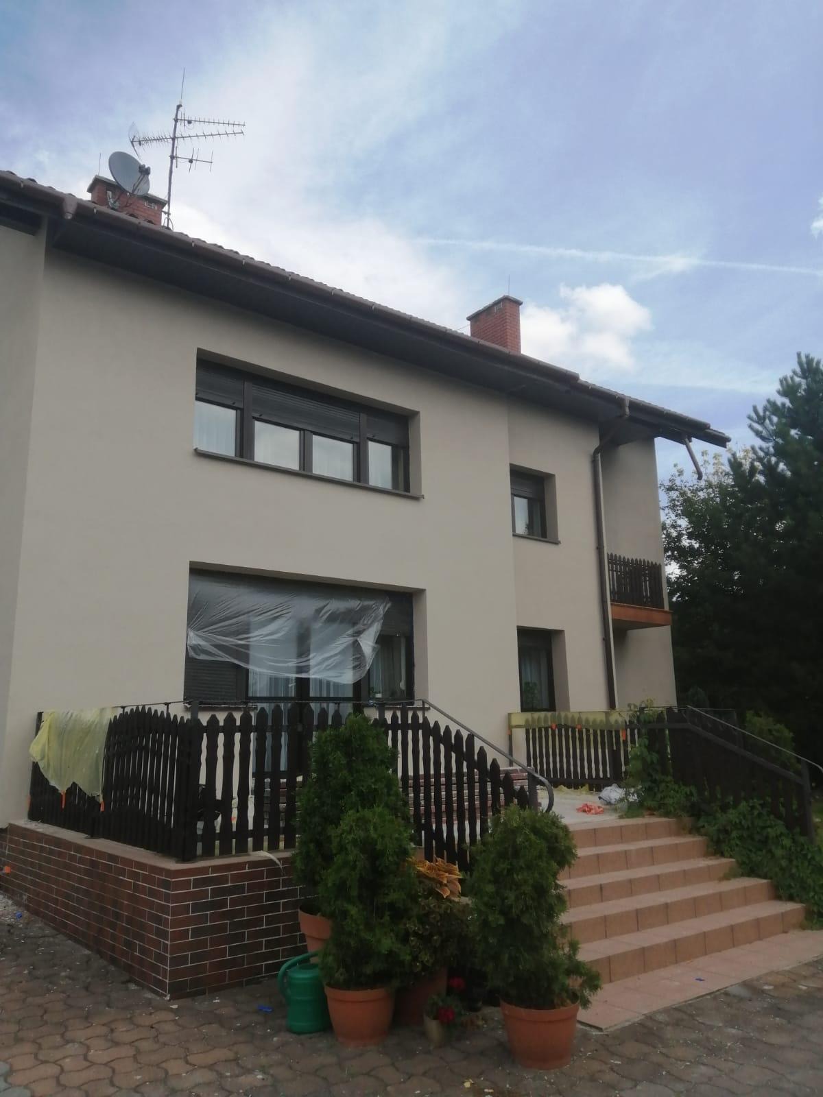 Elewacja domu po renowacji w Tychach, z widocznymi detalami jak okna z roletami i zabezpieczone folią okno. Świeżo pomalowana fasada.