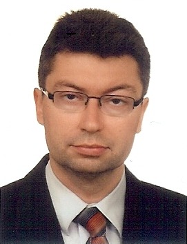 Portret mężczyzny w okularach i garniturze na białym tle. Zdjęcie biznesowe, neutralny wyraz twarzy, skierowany wprost do kamery. Profesjonalny wygląd.