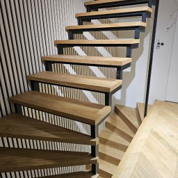 MPodłogi - Nowoczesne schody drewniane z czarną metalową konstrukcją, widok z góry na parkiet ułożony w jodełkę. Minimalistyczny design i naturalne materiały.