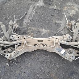 Libertad Robert Szydłowski - Element podwozia samochodowego, prawdopodobnie po piaskowaniu, leżący na szorstkiej powierzchni. Widoczne ślady korozji i zabrudzenia. Detal z warsztatu.