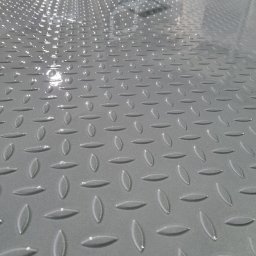 Libertad Robert Szydłowski - Błyszcząca, szara, metalowa powierzchnia z wytłoczonym wzorem łezkowym, prawdopodobnie po świeżym malowaniu. Widoczne odbicia światła.
