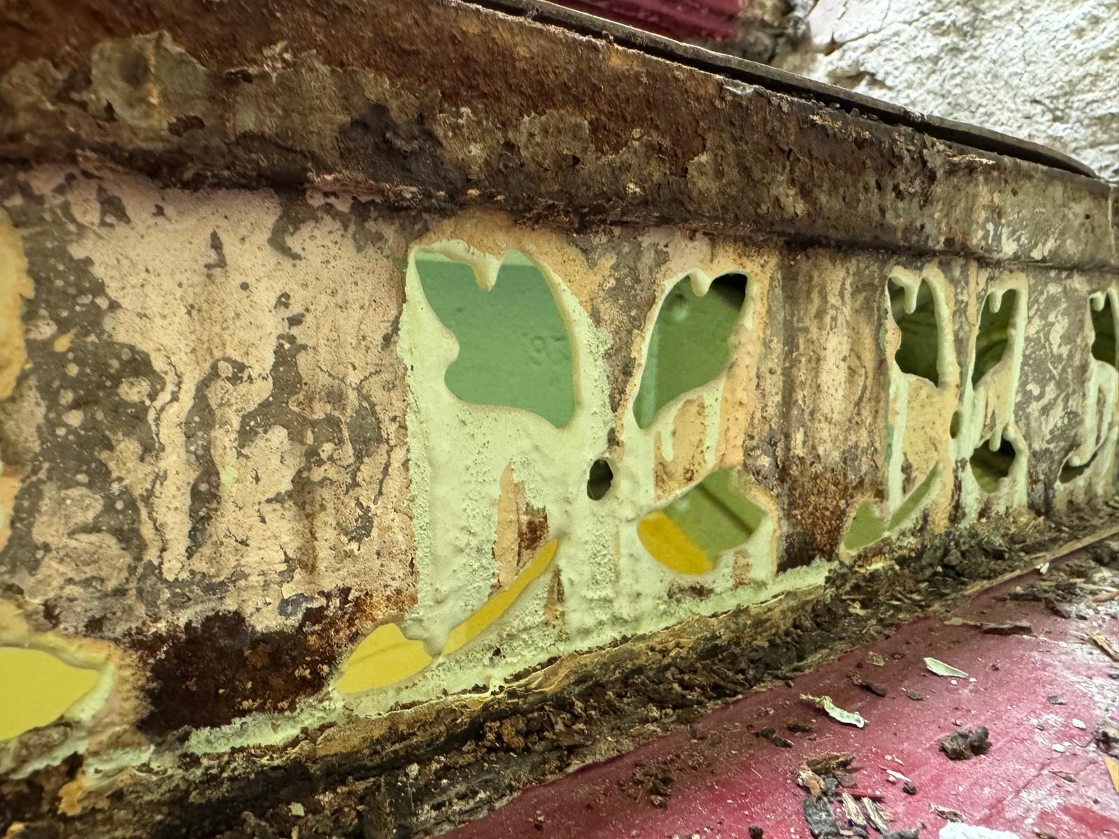 Zniszczona, skorodowana metalowa konstrukcja z resztkami farby i widocznymi śladami korozji. Detal z bliska ukazuje stopień degradacji materiału.