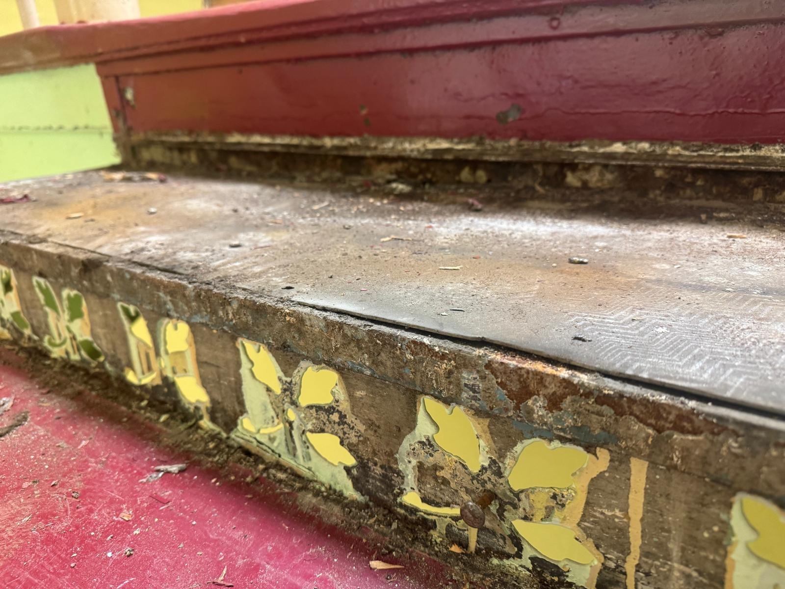 Zniszczone, drewniane schody z resztkami farby i dekoracji. Widoczne ślady użytkowania i zaniedbania. Detal z bliska, ukazujący zużycie i potrzebę renowacji.