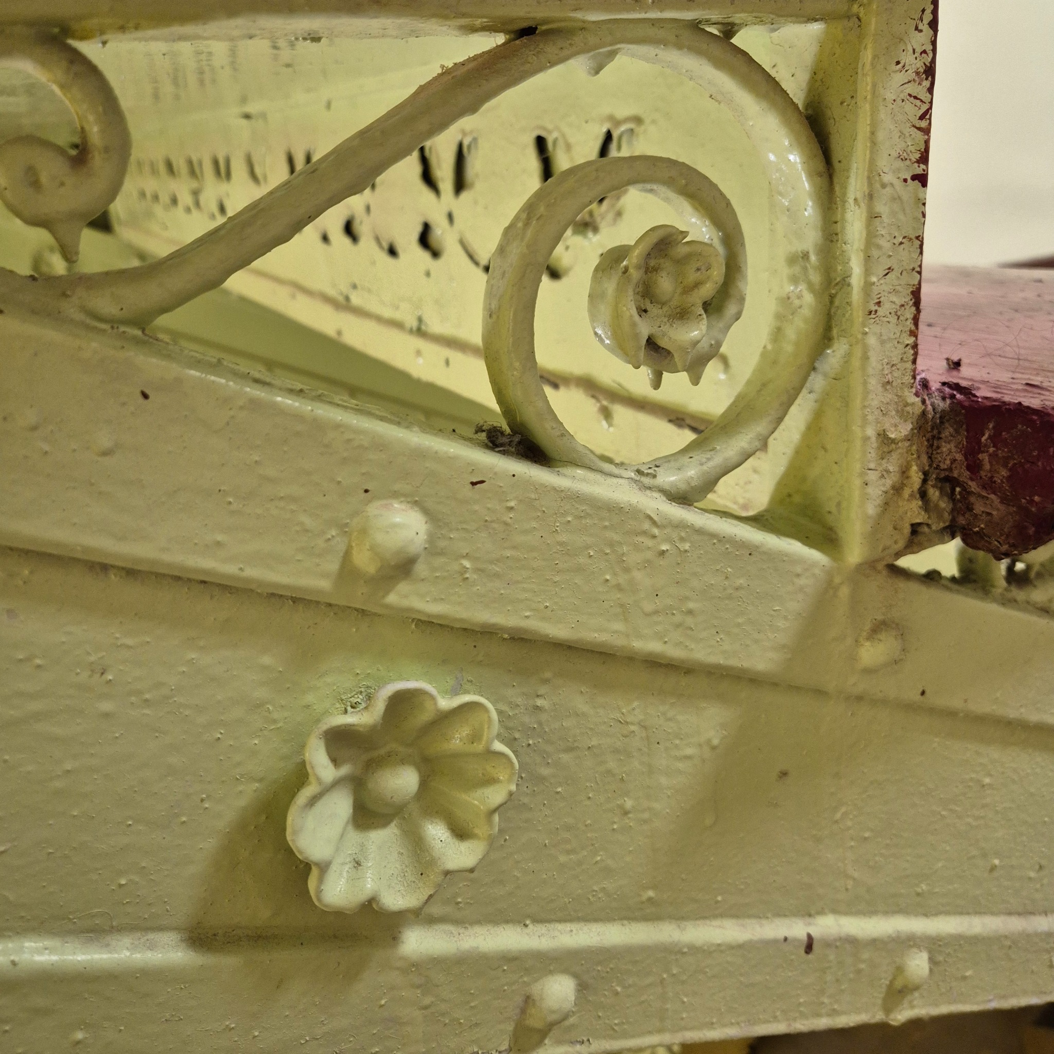 Kremowa balustrada schodowa z dekoracyjnymi elementami kwiatowymi i spiralnymi, widoczne ślady użytkowania i niedoskonałości farby.