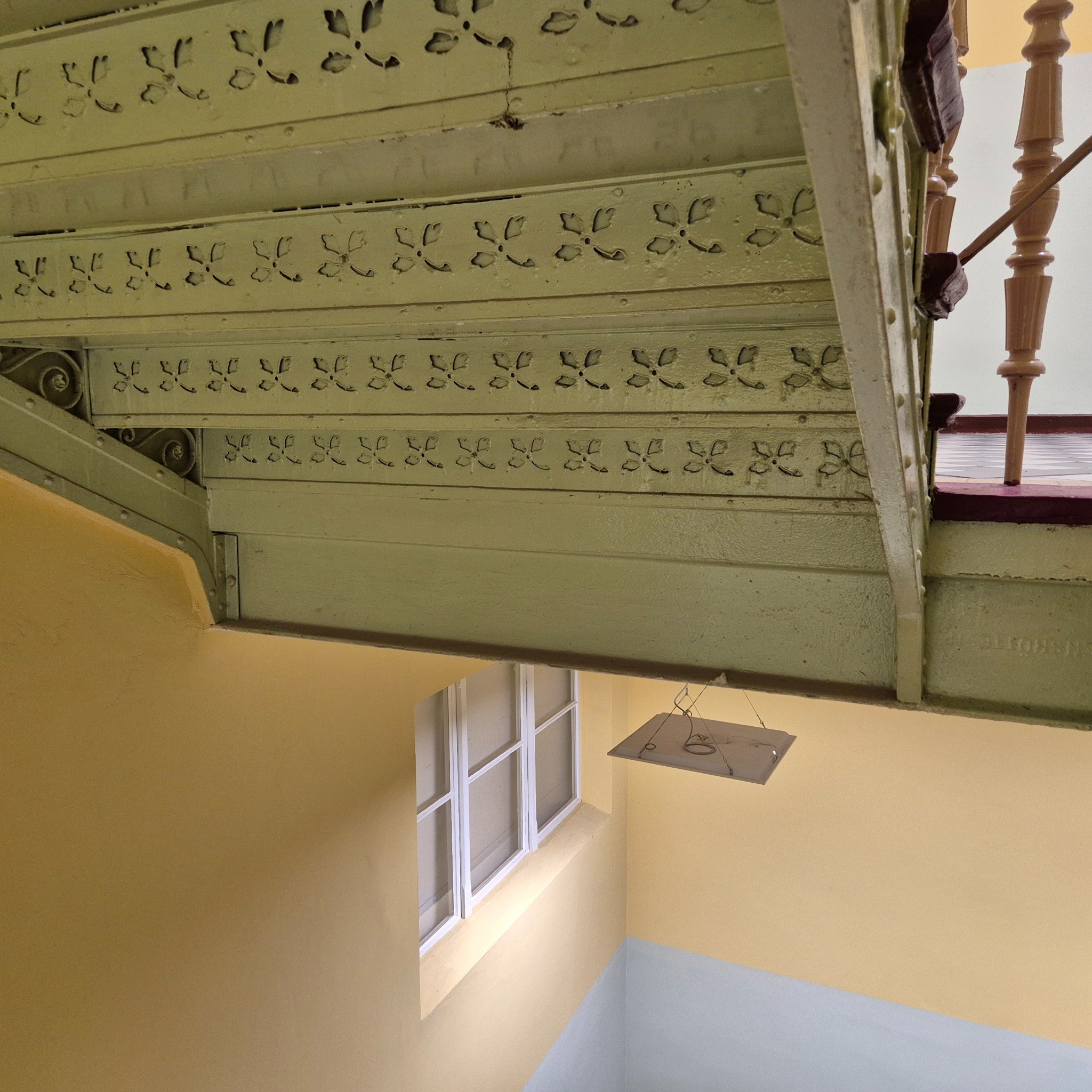 Metalowa konstrukcja schodów z dekoracyjnymi wycięciami, widok z dołu, oświetlenie naturalne, Wrocław. Elementy balustrady w tle.