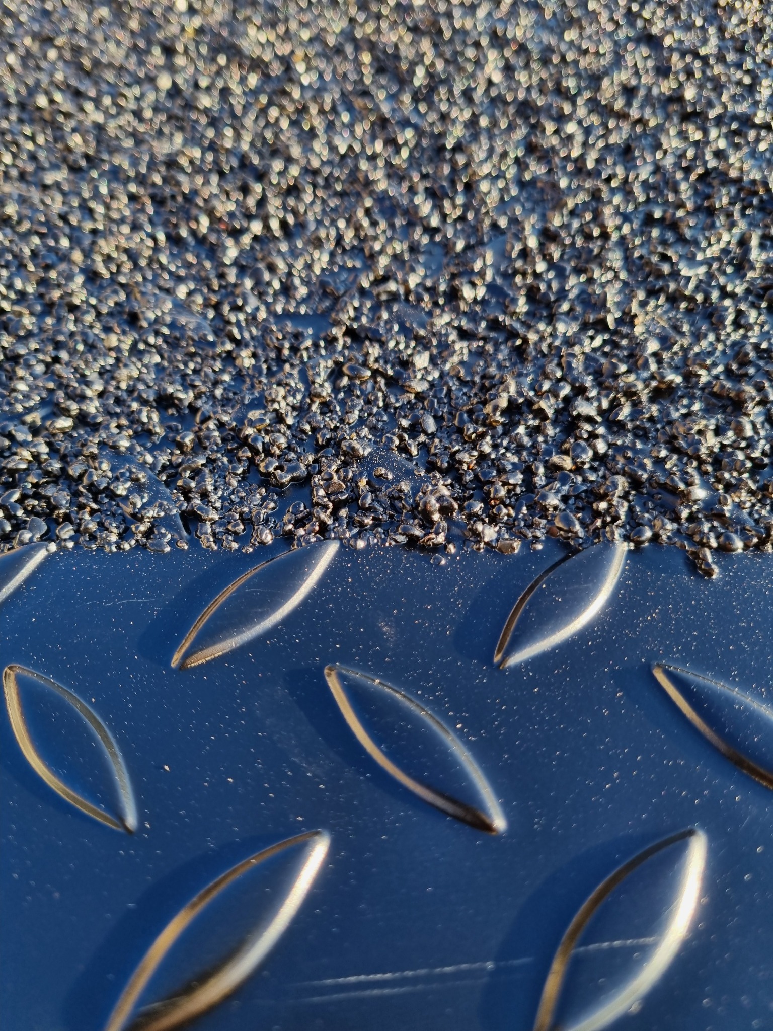 Metalowa powierzchnia z antypoślizgową powłoką, widoczne wypukłe wzory i drobinki. Detal zabezpieczenia antykorozyjnego, zbliżenie na fakturę i strukturę materiału.