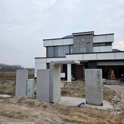 ProjectLab Dymitr Romanowski - Nowoczesna brama wejściowa z betonu architektonicznego przed domem, z numerem '59 Ceglana'. W tle widoczny budynek w trakcie prac wykończeniowych.